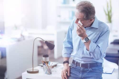 Man holding tissue to eye, in office wearing blue shirt and jeans