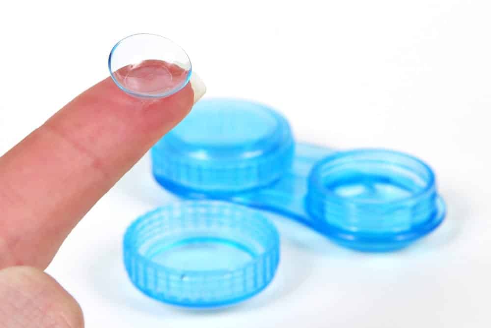 Finger holding contact lens, contact case in background