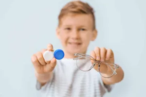 Young smiling boy holding out glasses and contact lens case