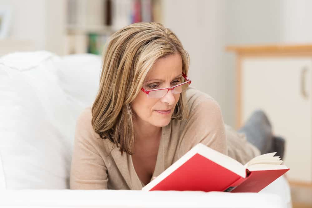 Middle-aged woman wearing glasses while reading on the couch