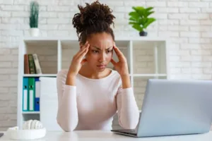 Woman pressing at head, looking at laptop