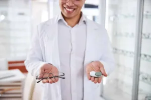 Optician smiling and holding out glasses in one hand and contacts in the other