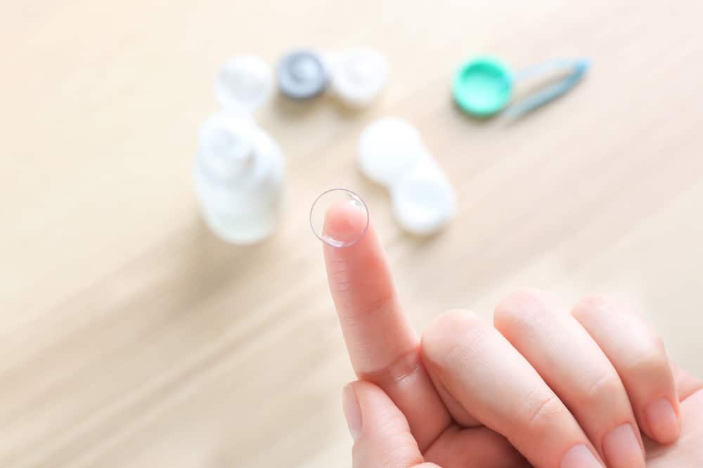 Finger holding contact lens, contact solution in background