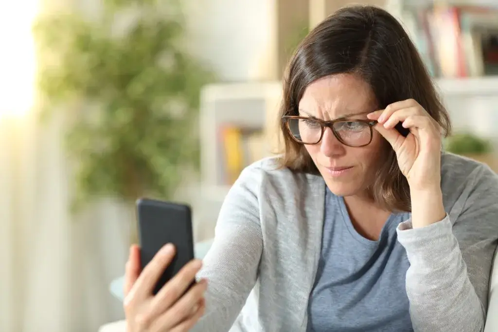 Woman wearing glasses squinting at her phone
