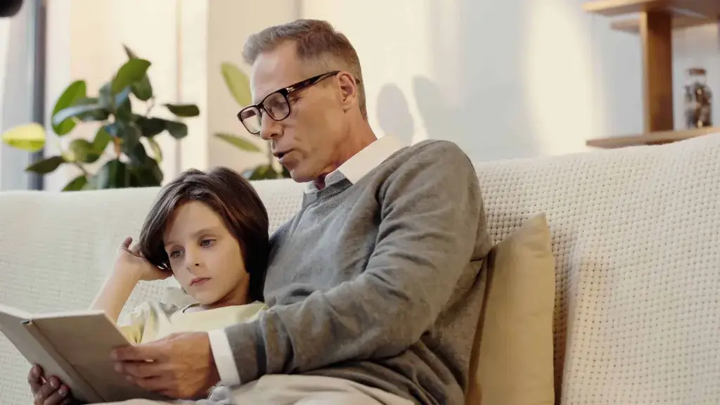 Senior man wearing reading glasses reading with child