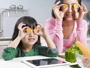 Young mother and daughter holding slices of carrot over their eyes