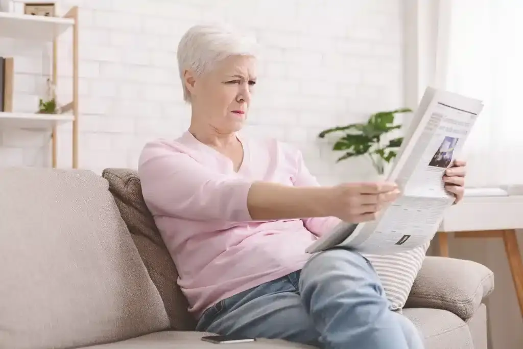 Senior woman squinting and holding newspaper back
