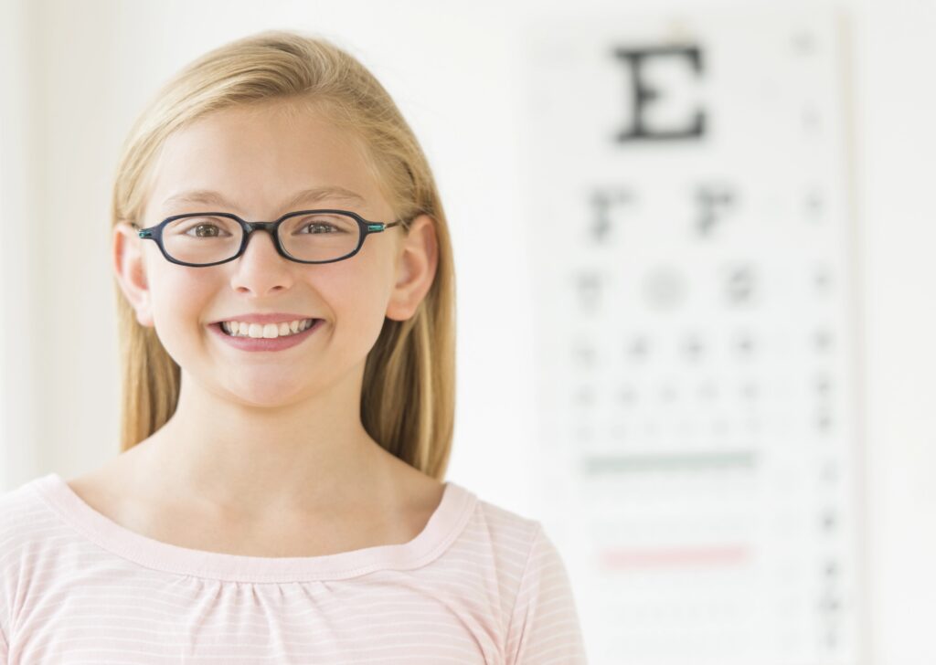 Young smiling girl wearing glasses in front of eye exam chart