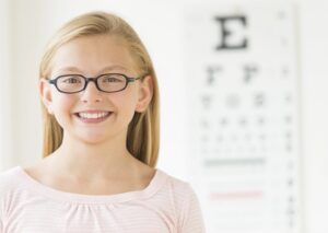 Young smiling girl wearing glasses in front of eye exam chart