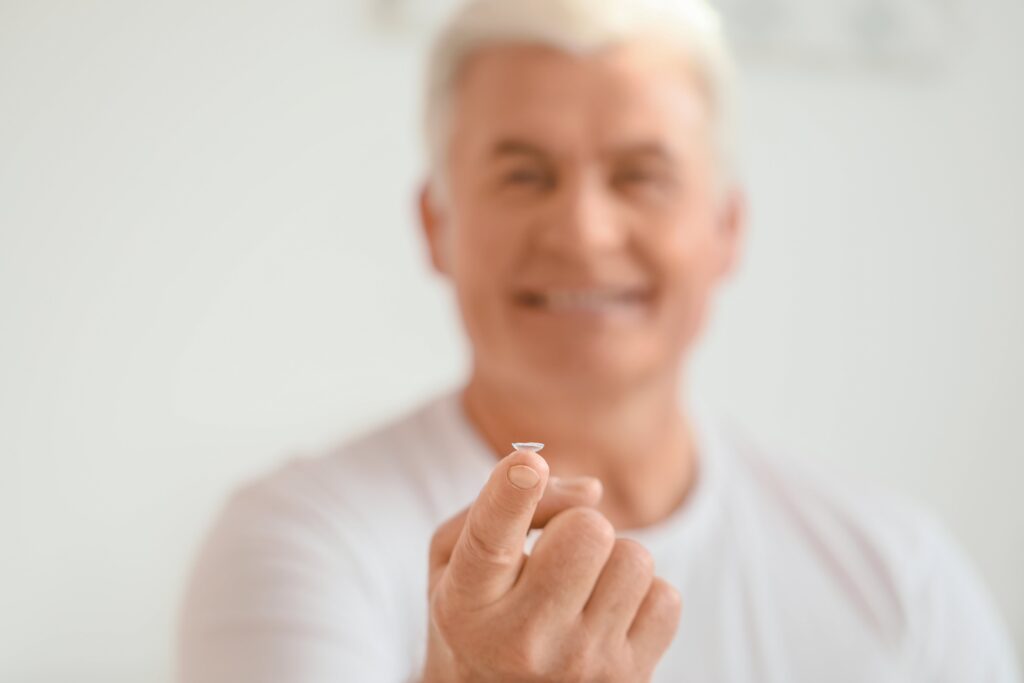 Senior man with arm stretched out, holding contact lens