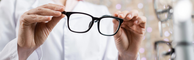 Cropped view of oculist in white coat holding eyeglasses in optics salon